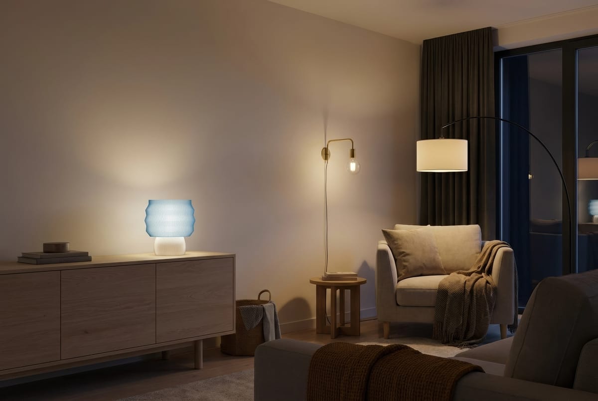 Stue om kvelden med en LEAH-bordlampe tent på skjenken, en gulvlampe over lenestolen og en vegglampe over et lite sidebord.