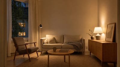 Stue om kvelden lyst opp i varmt 2700 K-lys fra en bordlampe og en gulvlampe, med varme skygger og en hvit vegg som gløder svakt gult.