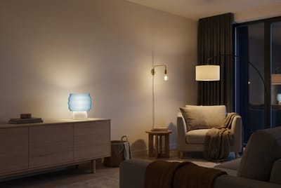 Stue om kvelden med en LEAH-bordlampe tent på skjenken, en gulvlampe over lenestolen og en vegglampe over et lite sidebord.